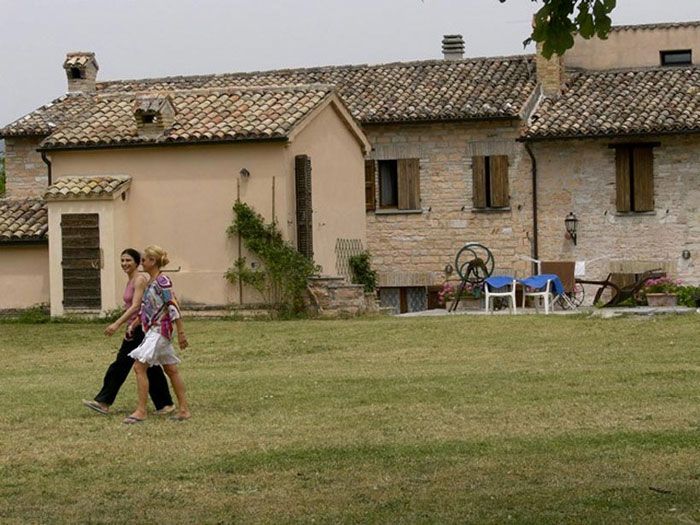 The stone farmhouse at Cà Le Suore, with people gathered on the grass in front of it.