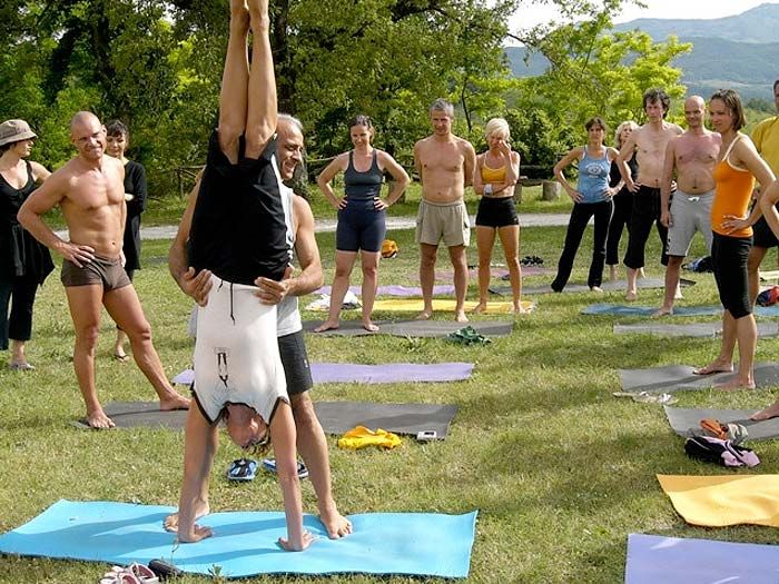A student in headstand on the grass at Cà Le Suore while the others look on, the hills behind.