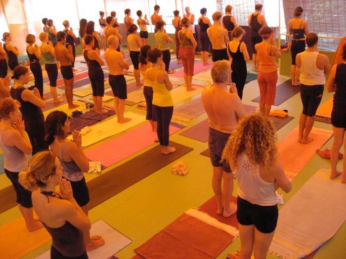 A led class in the shala at Kovalam, students standing on coloured mats between bamboo blinds.