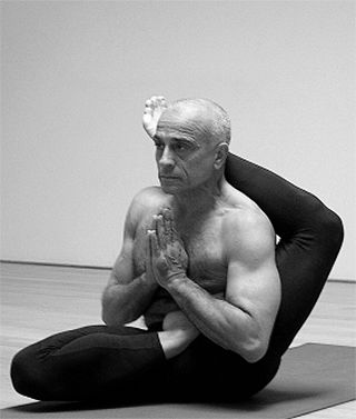Lino Miele seated on a mat, palms together at the chest in a bound seated posture.